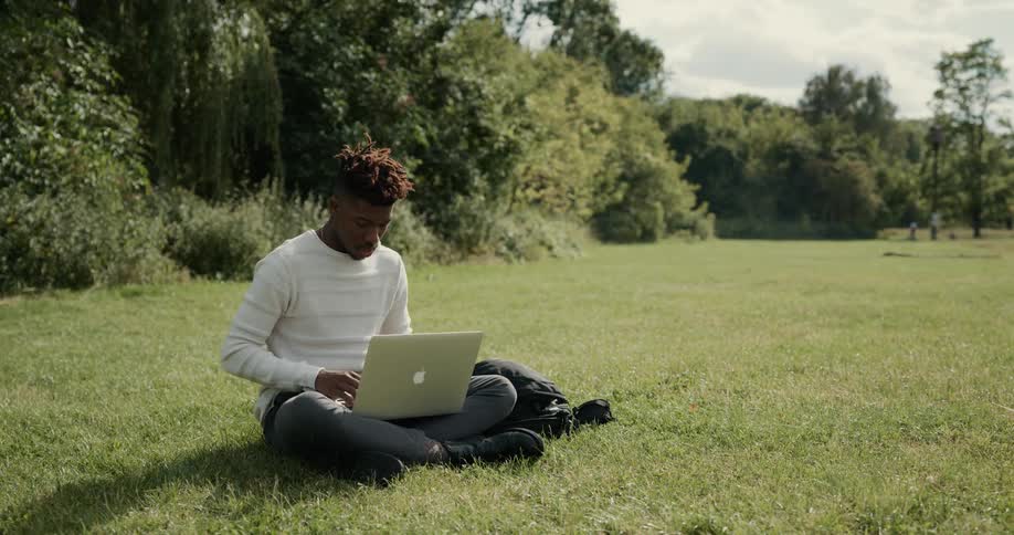A man is typing on his laptop and sitting in a field