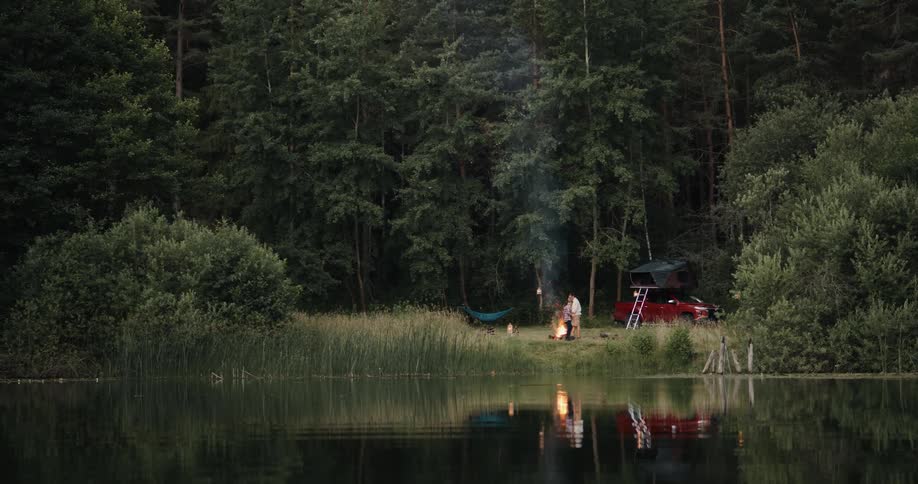 Father and son camping sitting around a campfire by the side of a lake in a forest