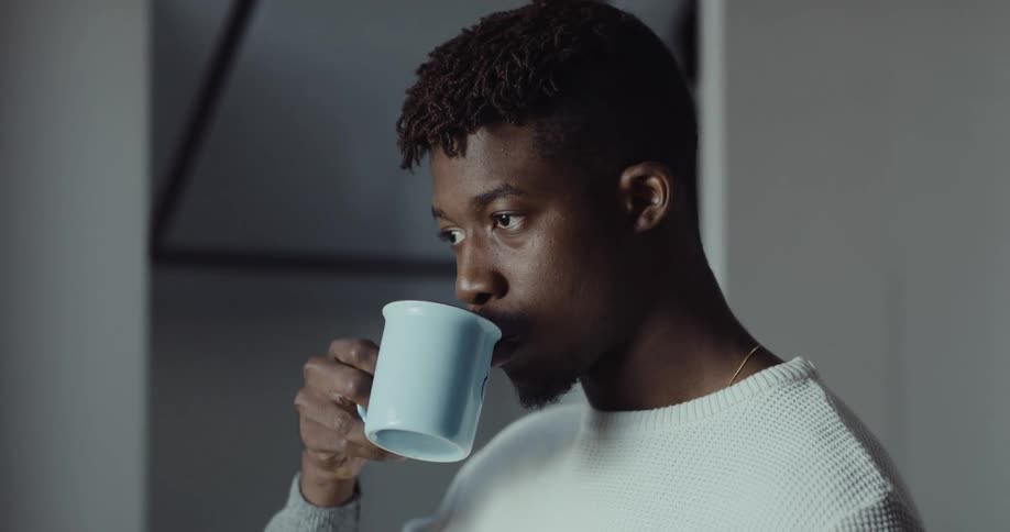 A man is standing in a room and drinking from a cup