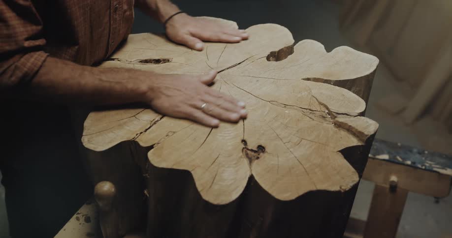 Wood carver runs hands over top of table carved from tree trunk