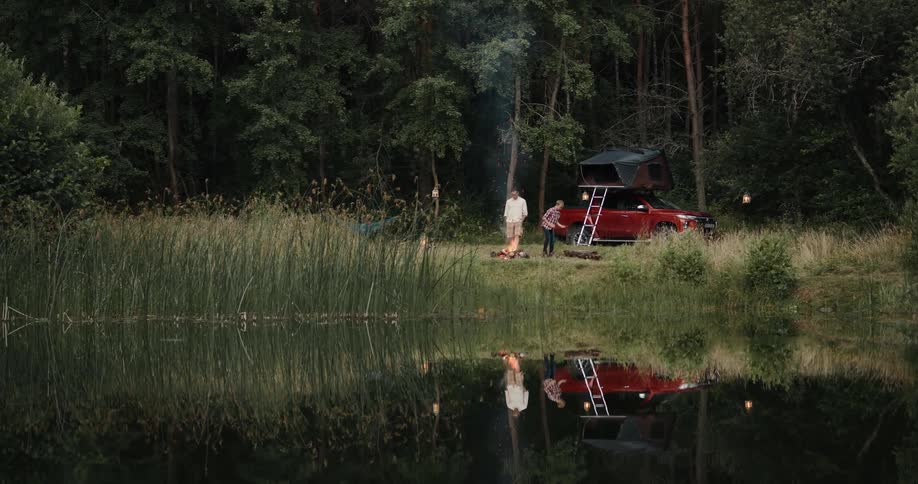 Father and son stand around campfire next to lake