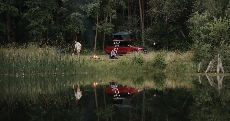 Father and son camp near lake and red car