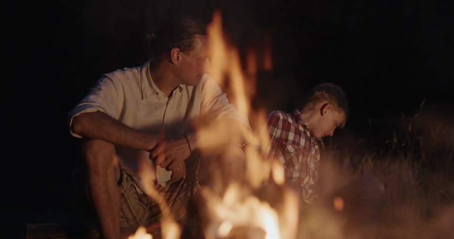A campfire sparks as a man and his son talk