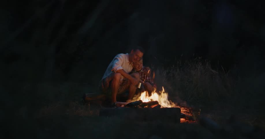 A father and son sitting outside near a campfire