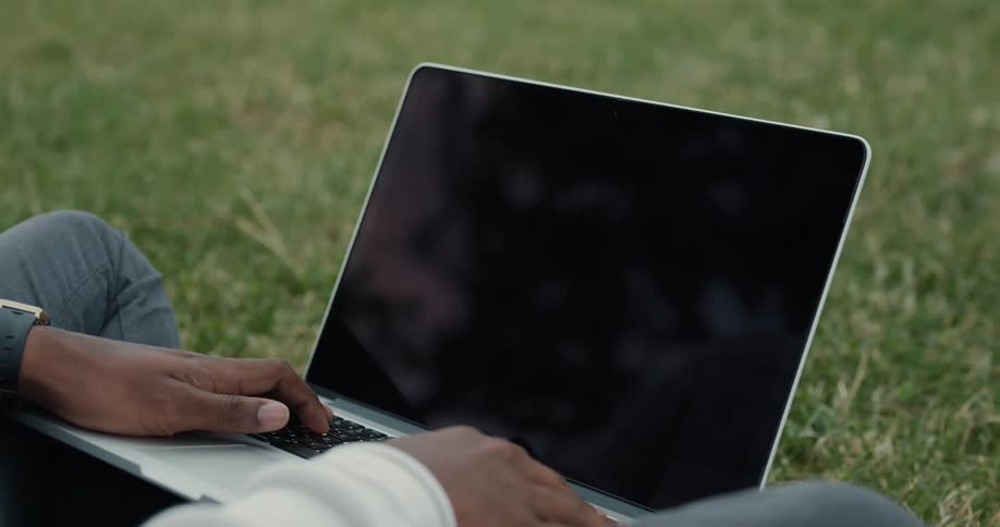 A person is sitting in a grassy field with a laptop