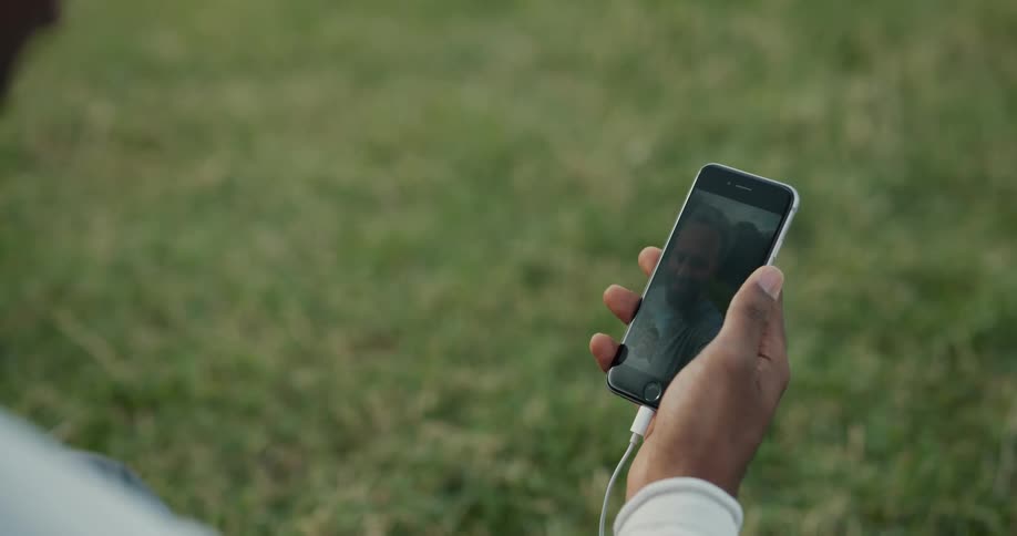 A man is standing outside in a field holding a cell phone in his hand