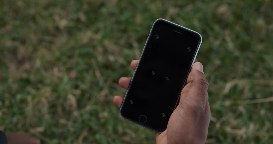 Black mans hand holding a smartphone in front of the grass outdoors during daylight
