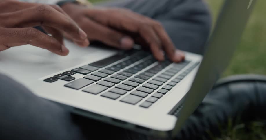 Person sits in field typing on laptop