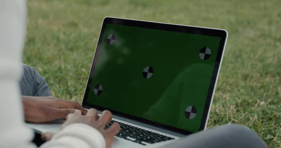 A man is sitting outside on the grass typing on a laptop computer