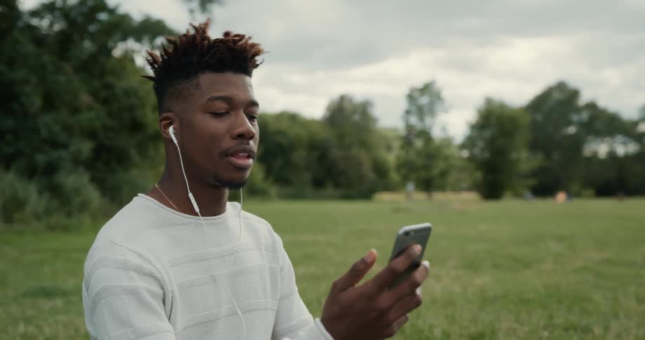 A man sits in a large open lawn space talking on a cell phone