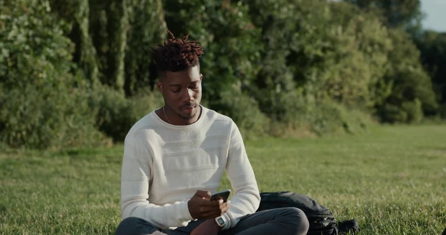 A man is sitting in a field and checking his cellphone