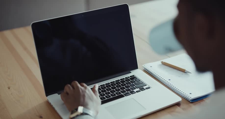 A man is sitting indoors and typing on a laptop