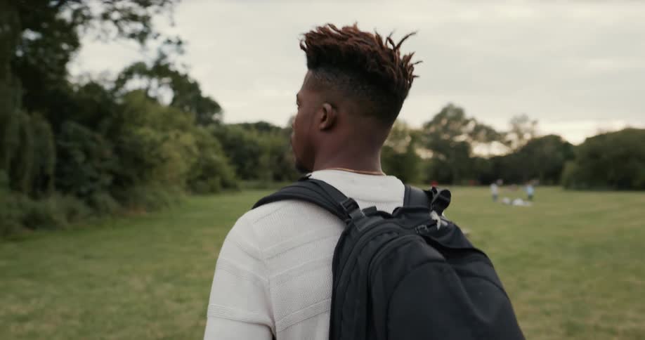 A man is walking through a field and sits on the grass