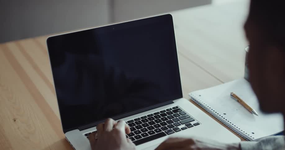 A man is typing on a laptop at his computer desk