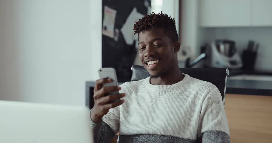 A man is sitting indoors and talking on his cellphone