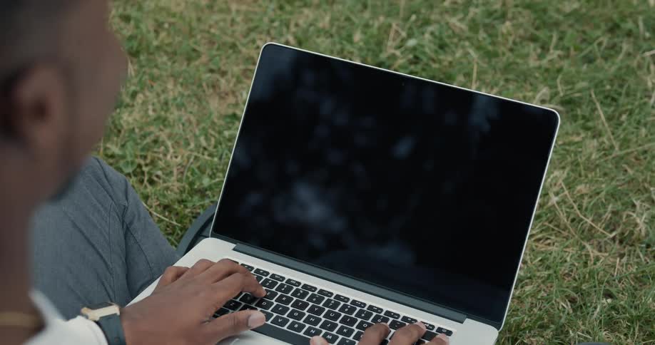 A man is sitting outdoors with his laptop