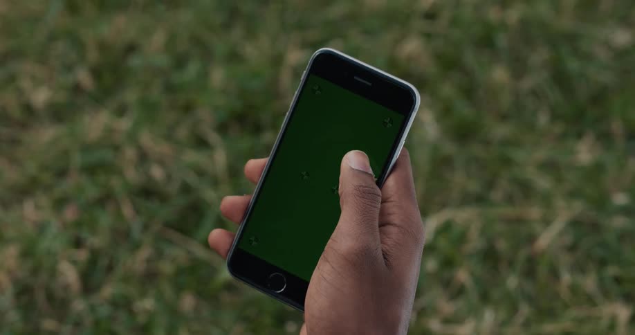 A man holds his phone and touches the screen over grass