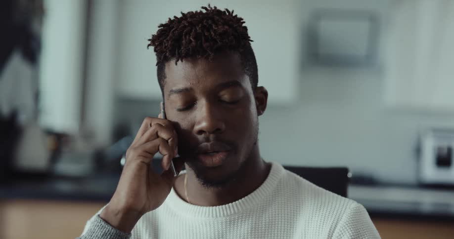 A man is sitting at a kitchen table talking on the phone