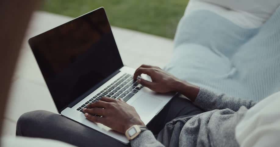 A person is sitting outdoors and typing on a laptop