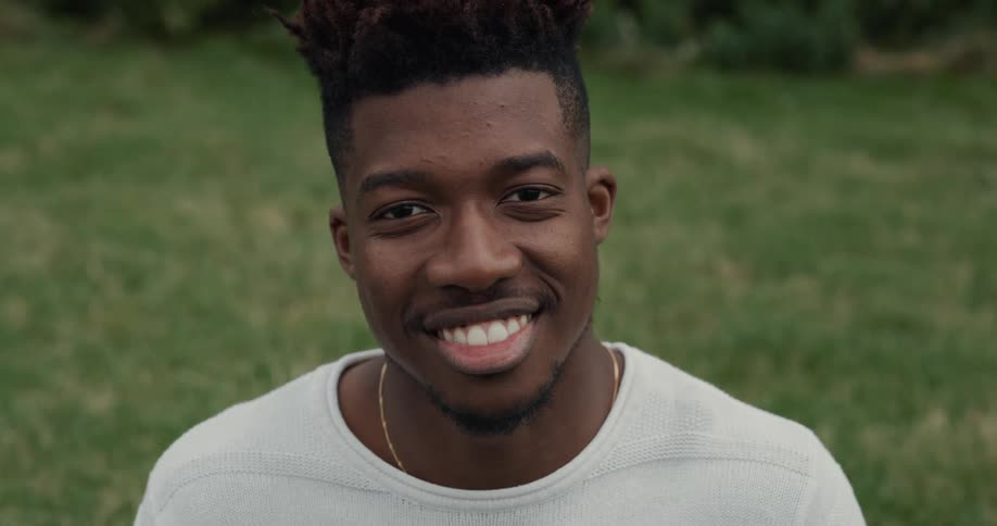 Young black man sitting on the grass at a sunny day and smiling