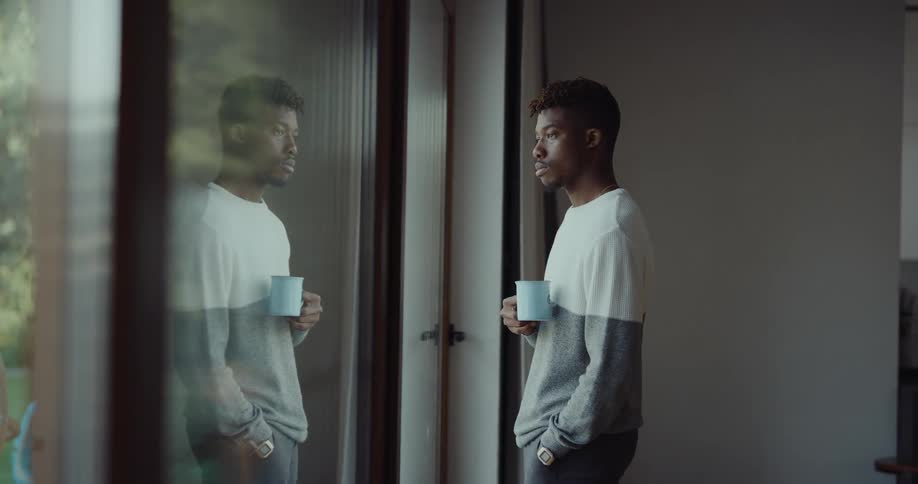A man is drinking a cup of coffee and looking out a window