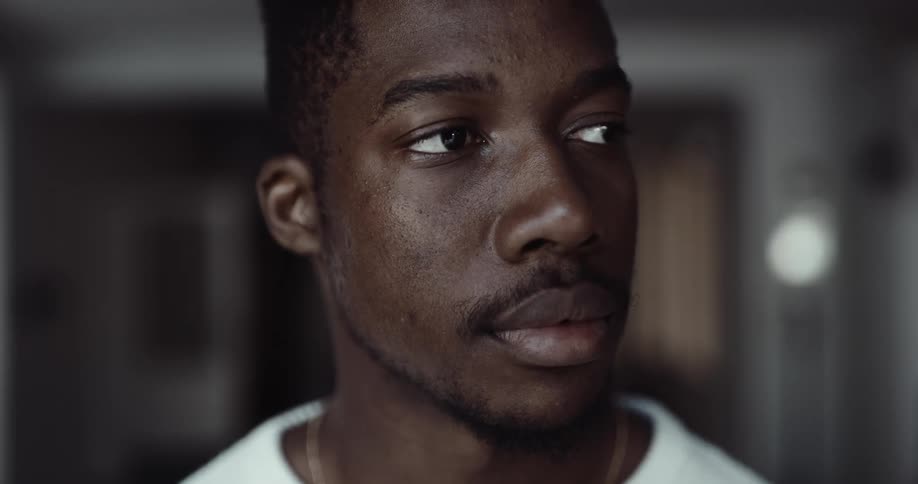 Black man standing indoors looking around and drinking a cup of coffee