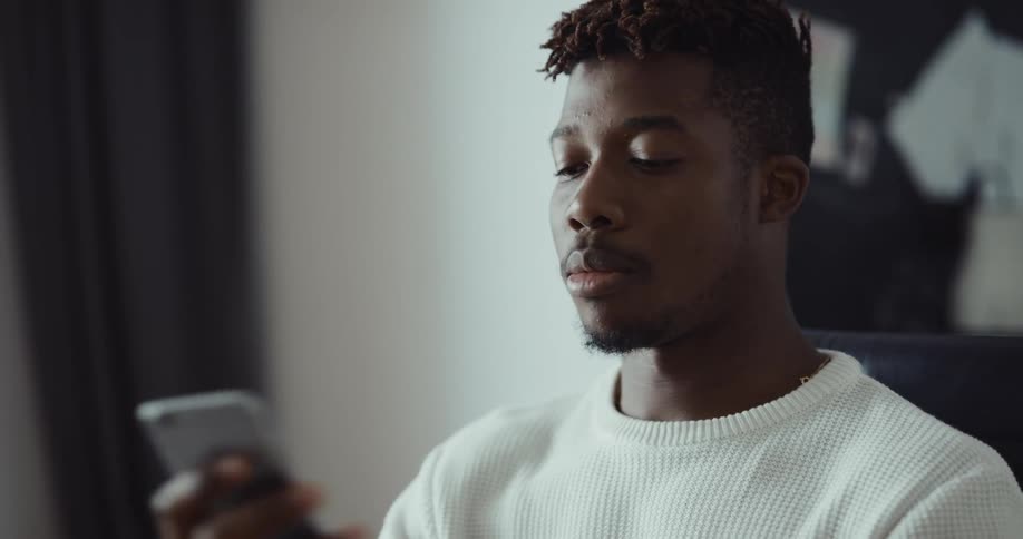 A man is sitting indoors and talking on his phone