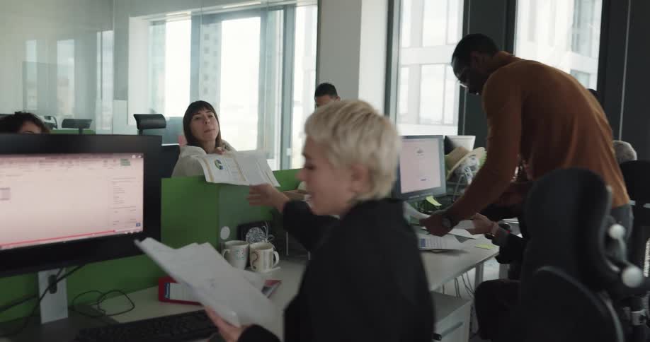 Businesspeople sitting at desks work and talk to each other