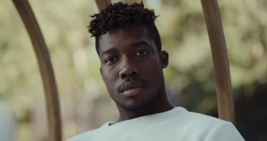 Head and face of a young black man sitting on a swing chair outside