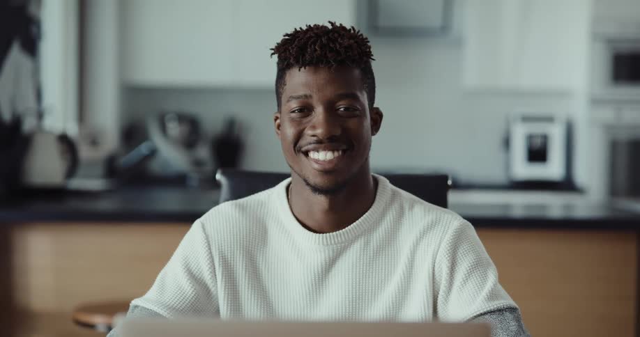 A man looks up to smile into the camera while sitting indoors during the day