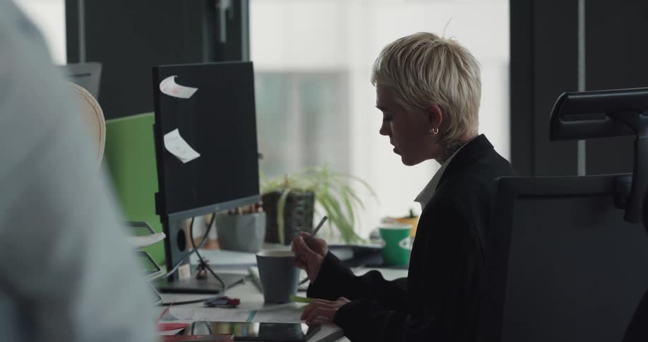 Young blonde woman working on her desk at the office and then standing while picking up a call on her phone