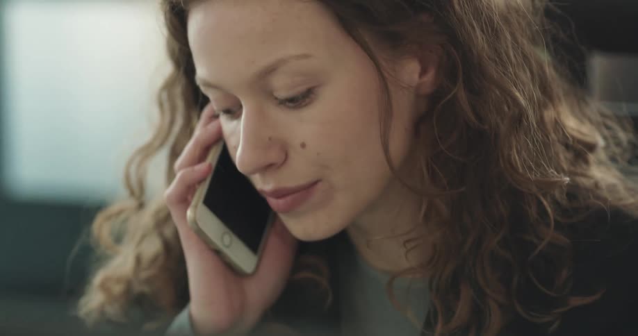 A woman is sitting indoors and talking on her cellphone