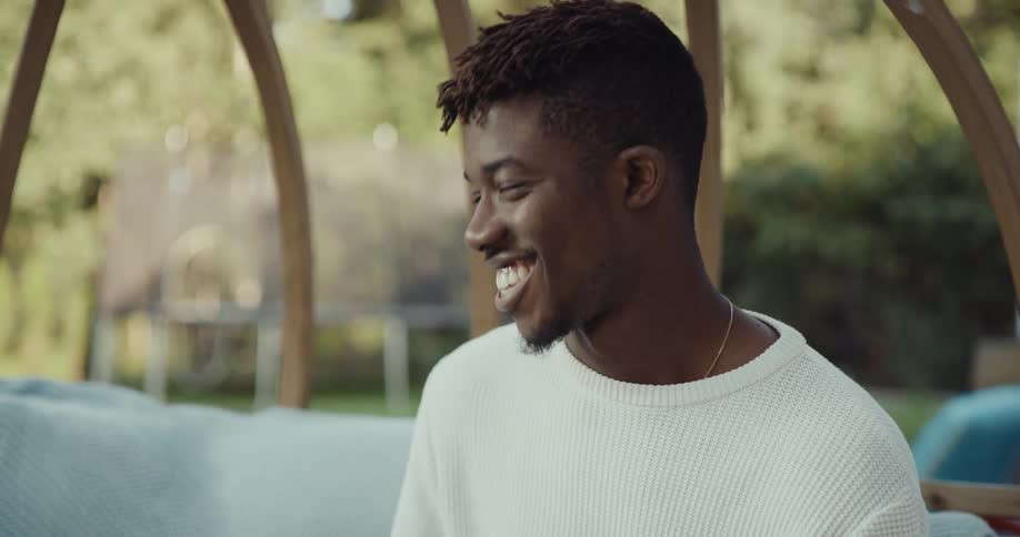 Happy and relaxed young black man sitting in a swing chair in his backyard drinking a cup of coffee