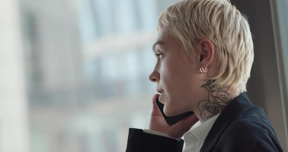 Female office worker standing next to big glass windows talking on the phone