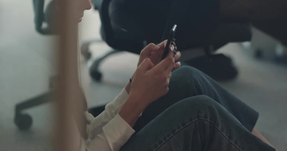 Woman with straight hair shirt and jeans uses smartphone at the office