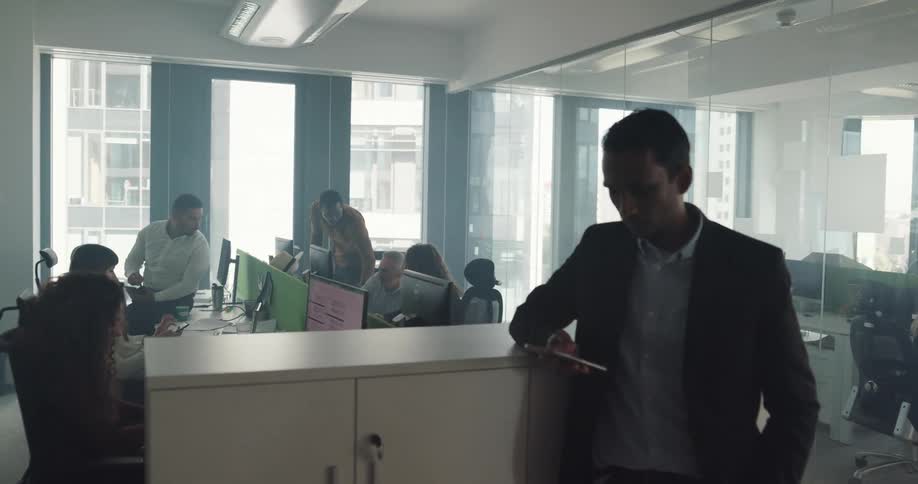 An office employee stands at the end of a table looking at his cell phone