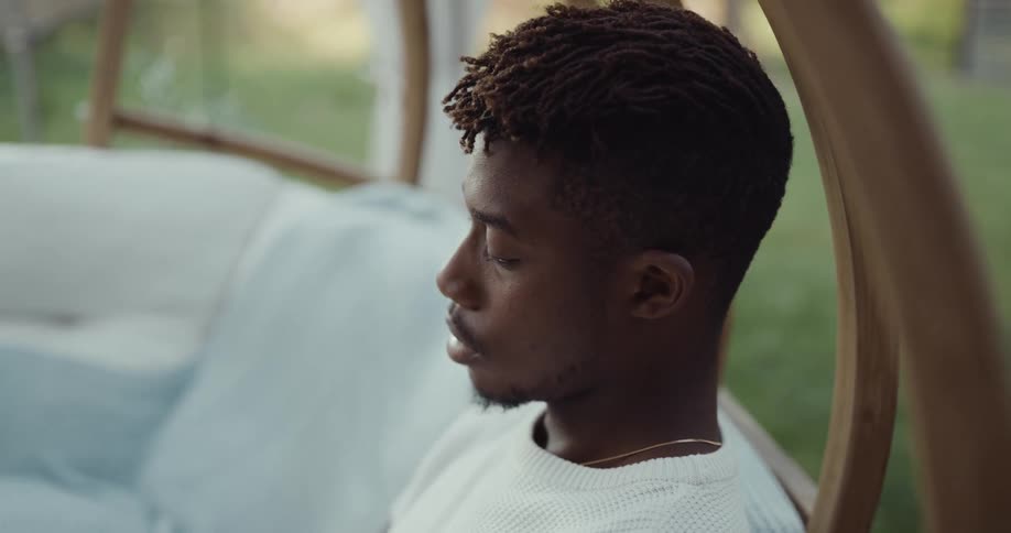 Young man leisurely sitting on a couch in the backyard working on a laptop