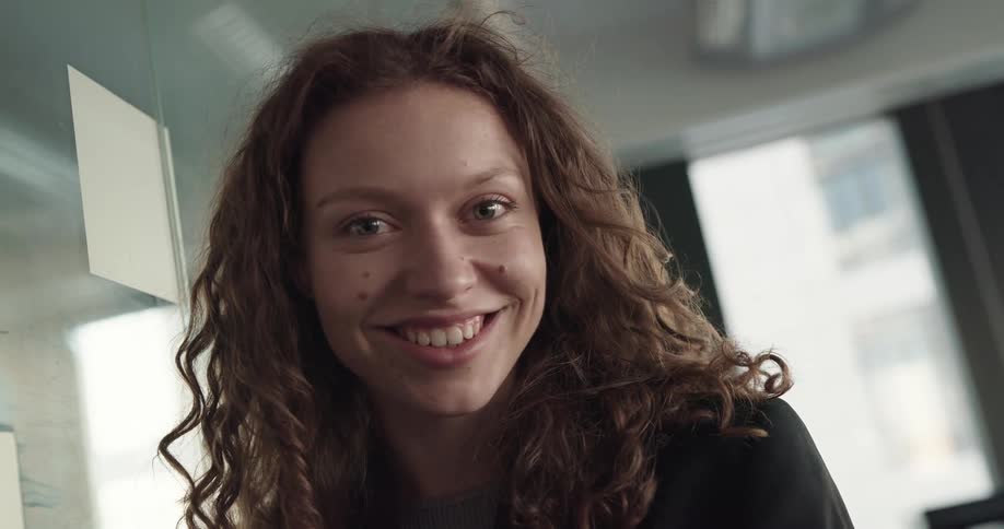 Young woman with curly hair standing in an office space and smiling