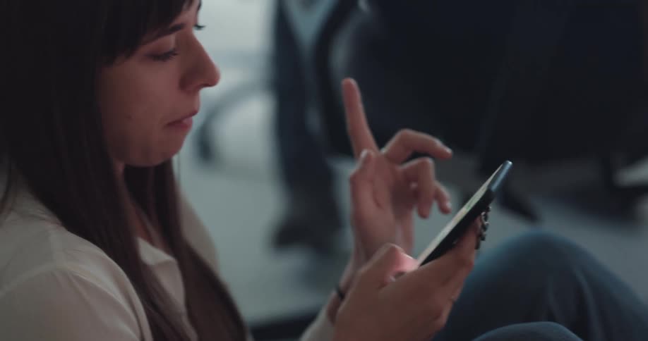Woman with straight hair white shirt and jeans sits on ground using smartphone at the office