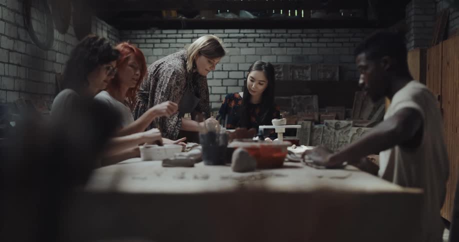 A group of people mold clay together at a table indoors during the day