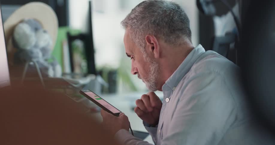 A man is sitting indoors and texting on his cellphone
