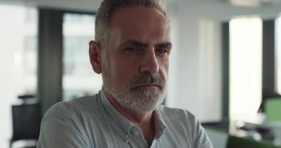 Businessman with beard and blue shirt smirks at camera at the office