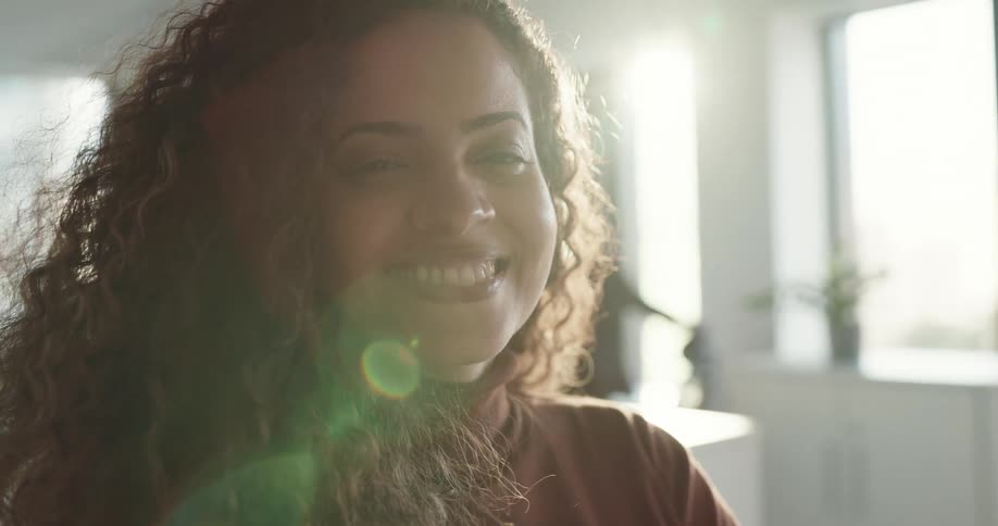 A woman turns her head to smile into the camera while sitting indoors during the day