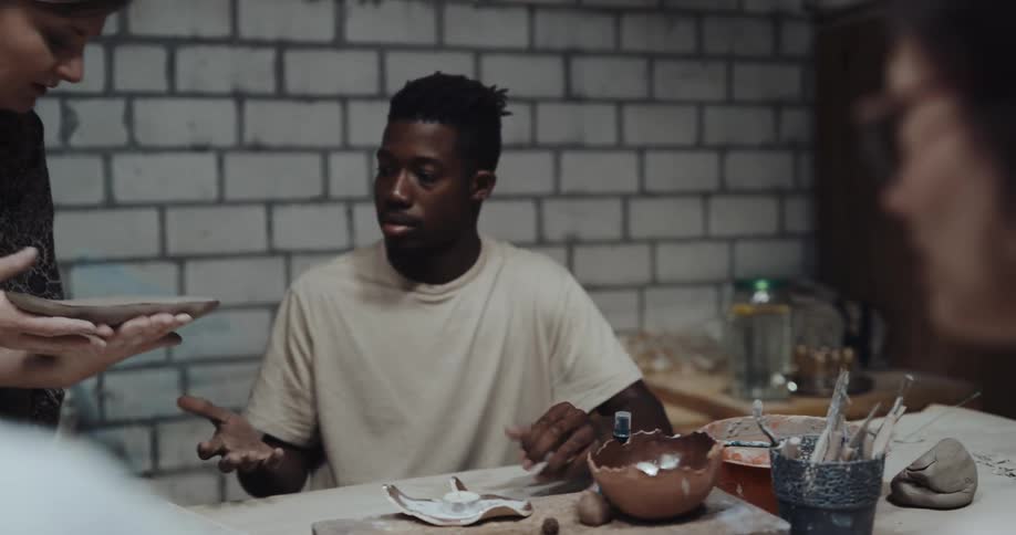 A woman cuts a piece of clay and hands it to a man