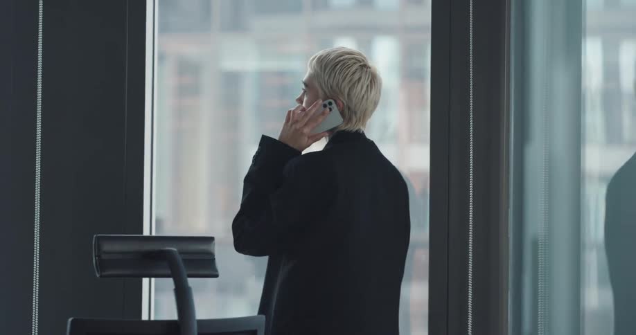 A man answers a phone call at her office desk and gets up to look out of the window while talking