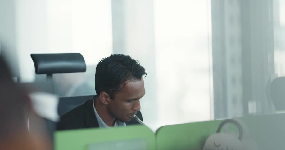 Young man sitting at his desk next to the window working in the office and drinking a cup of coffee