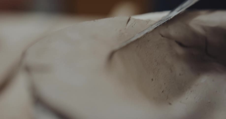 Hands hold clay still and trim the edge from the mold