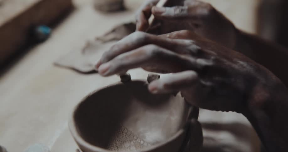 A man sculpts edges onto a clay bowl