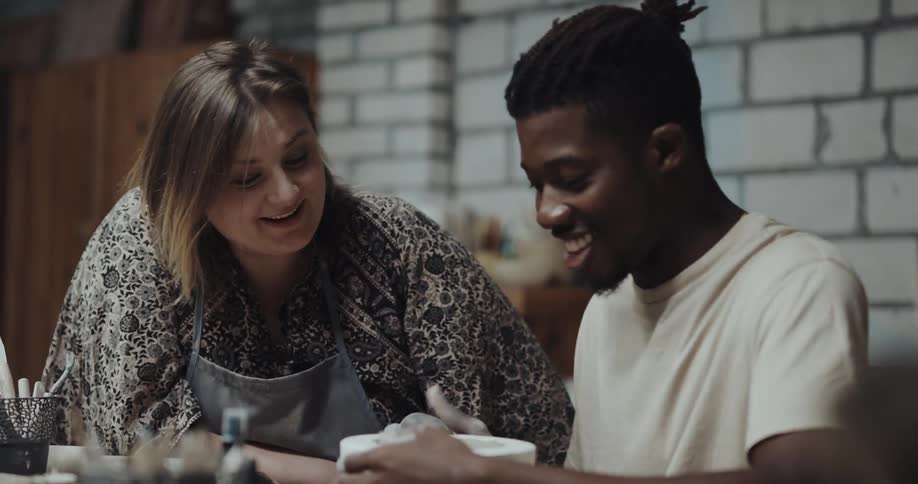 A pottery teacher chats with a student while he makes a bowl