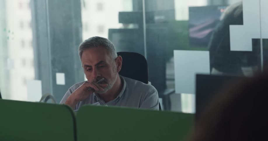 Man sits at work desk as woman passes by behind him